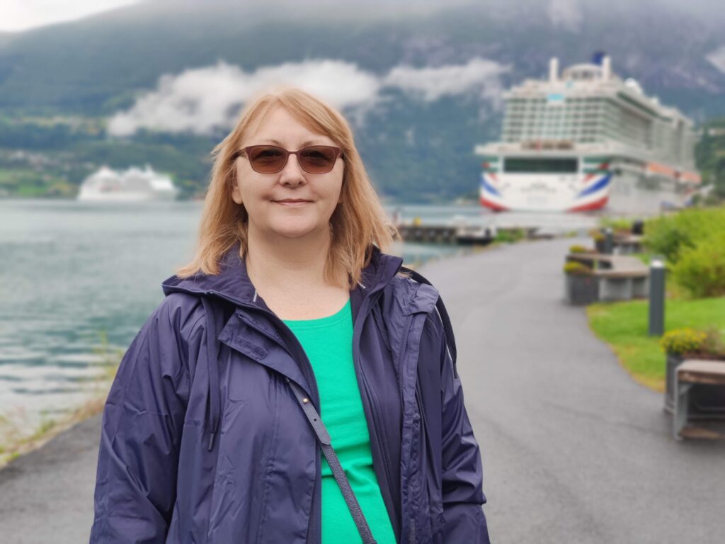 Fi Phillips standing in a Norwegian setting with the cruise ship Iona in the background