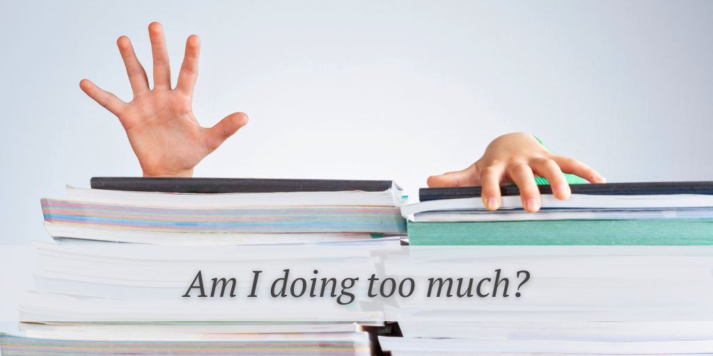 someone struggling behind a pile of papers and books and the words am I doing too much?